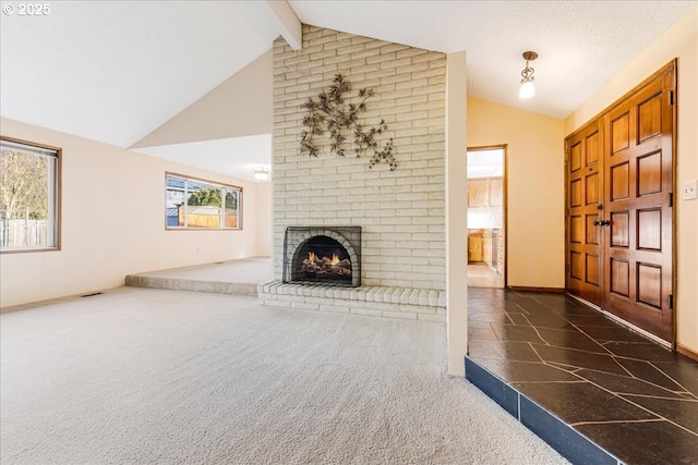 unfurnished living room with a healthy amount of sunlight, a fireplace, dark carpet, and vaulted ceiling with beams