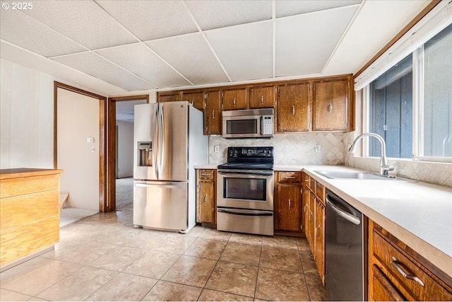 kitchen with appliances with stainless steel finishes, decorative backsplash, a drop ceiling, sink, and light tile patterned flooring