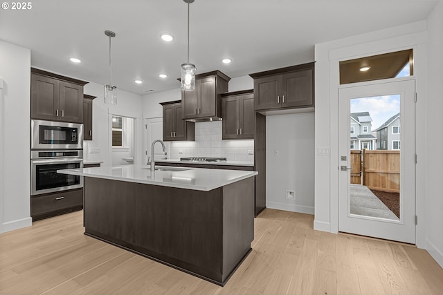 kitchen featuring dark brown cabinetry, decorative light fixtures, a kitchen island with sink, and stainless steel appliances