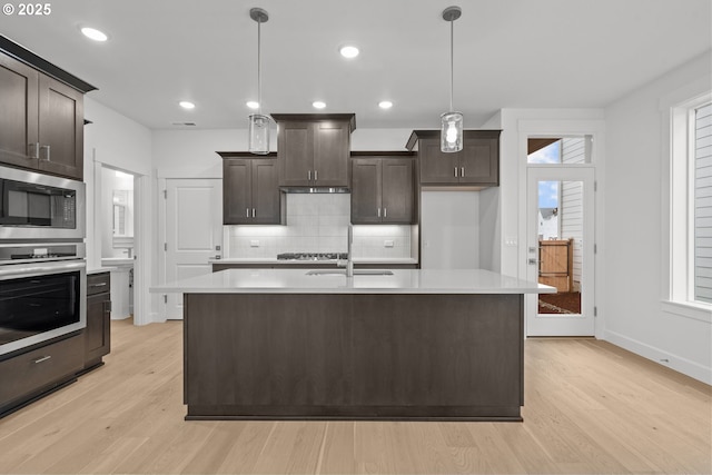 kitchen with pendant lighting, dark brown cabinetry, stainless steel appliances, and an island with sink