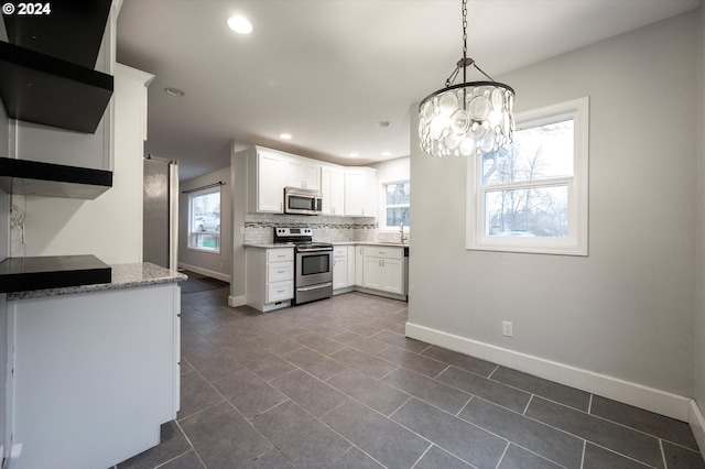 kitchen with backsplash, appliances with stainless steel finishes, decorative light fixtures, white cabinetry, and a chandelier