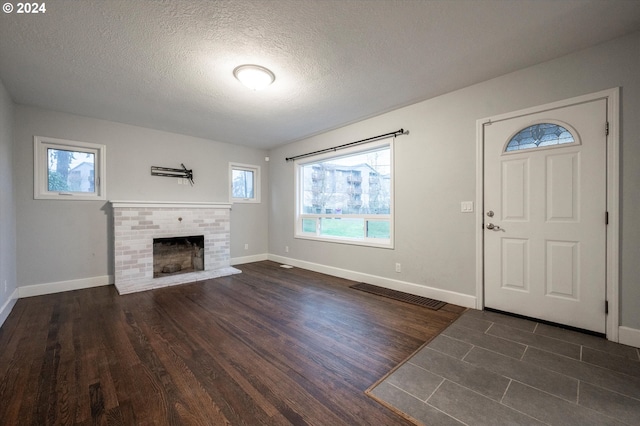 entryway with dark wood-type flooring, a textured ceiling, and a brick fireplace