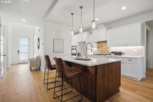 kitchen with decorative backsplash, a kitchen breakfast bar, light countertops, white cabinetry, and light wood finished floors