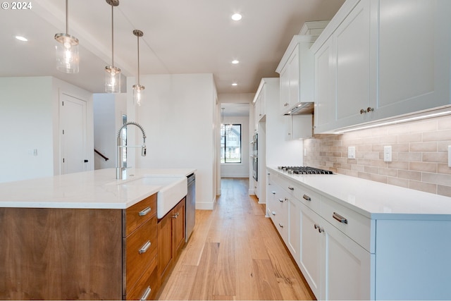 kitchen featuring light hardwood / wood-style flooring, decorative light fixtures, sink, white cabinets, and an island with sink