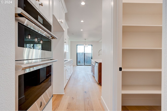 kitchen with white cabinets, light hardwood / wood-style flooring, pendant lighting, and appliances with stainless steel finishes