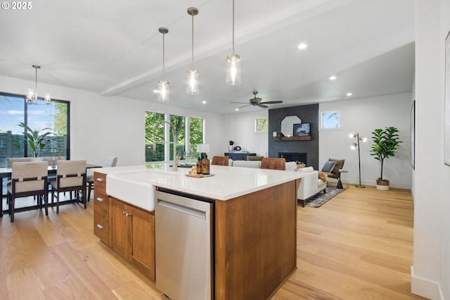 kitchen featuring brown cabinetry, a large fireplace, stainless steel dishwasher, ceiling fan with notable chandelier, and light wood-style flooring