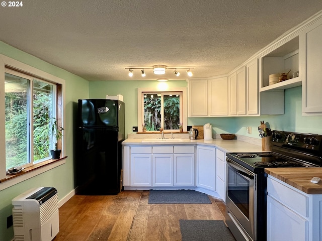 kitchen featuring stainless steel electric range, black refrigerator, sink, light hardwood / wood-style flooring, and white cabinetry