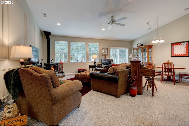 carpeted living room featuring a wood stove and ceiling fan with notable chandelier