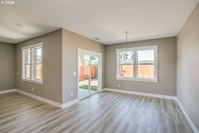 unfurnished dining area with light wood-type flooring and an inviting chandelier