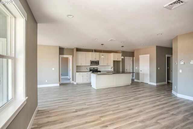 kitchen with white cabinets, stainless steel appliances, light hardwood / wood-style floors, decorative backsplash, and pendant lighting