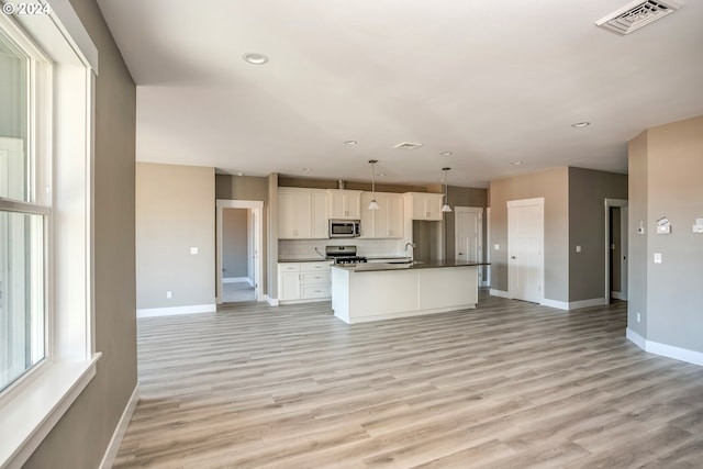 kitchen featuring appliances with stainless steel finishes, decorative light fixtures, white cabinets, a kitchen island with sink, and light hardwood / wood-style floors