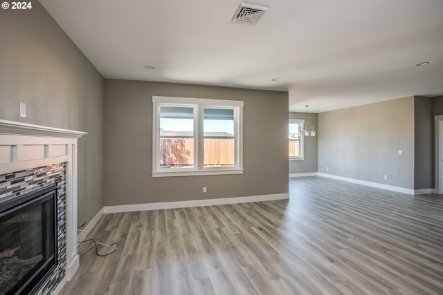 unfurnished living room featuring a stone fireplace, a chandelier, and light wood-type flooring