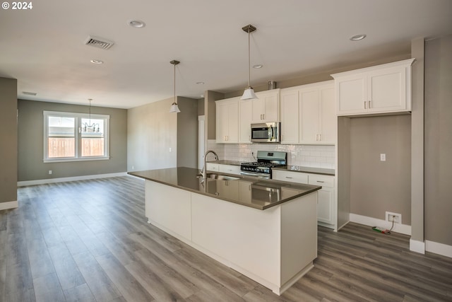 kitchen with stainless steel appliances, white cabinetry, and an island with sink