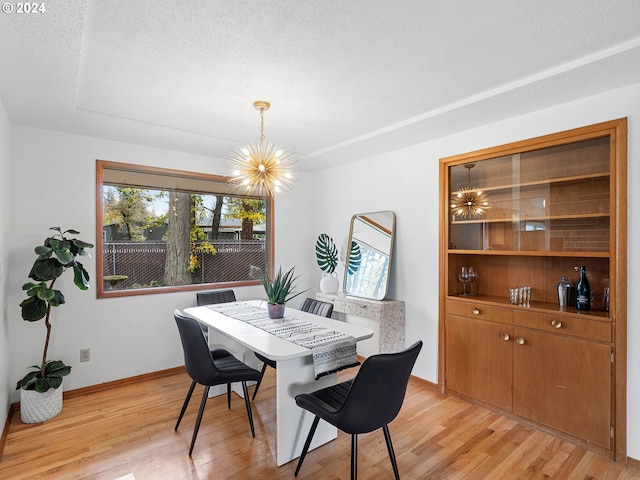 dining space with light wood-style floors, a notable chandelier, a textured ceiling, and baseboards