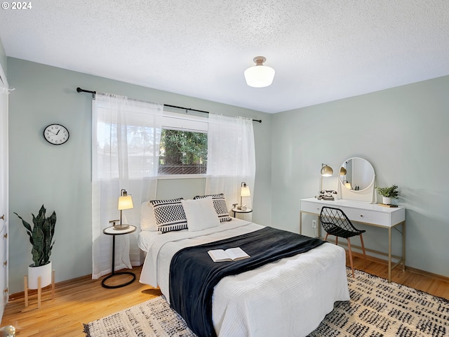 bedroom with a textured ceiling, light wood-type flooring, and baseboards