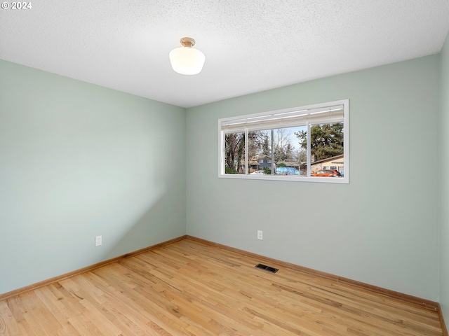 spare room featuring light wood-type flooring, visible vents, a textured ceiling, and baseboards