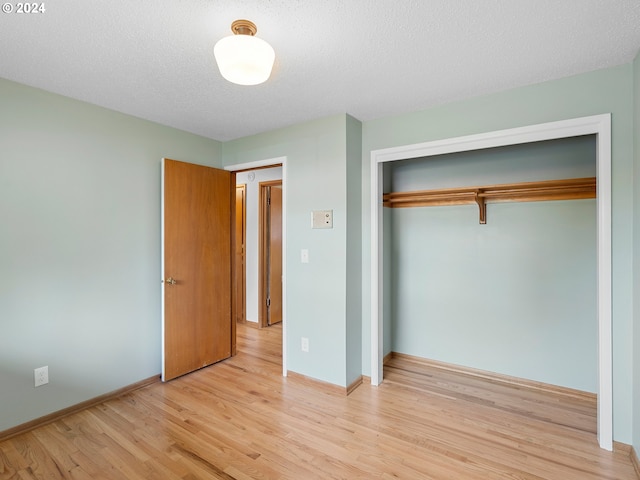 unfurnished bedroom featuring light wood-type flooring, a closet, a textured ceiling, and baseboards