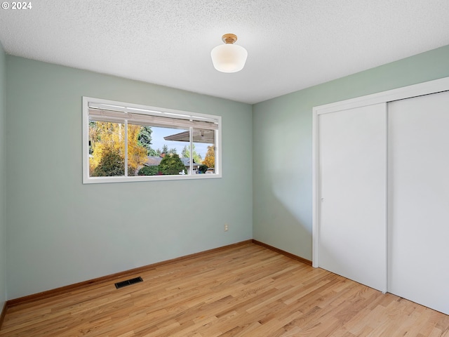 unfurnished bedroom with light wood-type flooring, a textured ceiling, and a closet