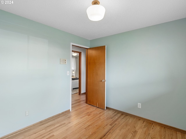 spare room with a textured ceiling, light wood-type flooring, and baseboards