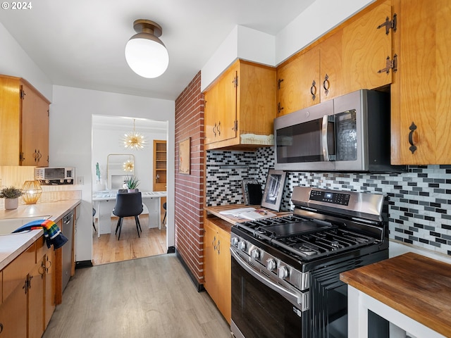 kitchen with backsplash, stainless steel appliances, light wood-type flooring, and an inviting chandelier