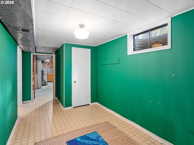 basement with baseboards, water heater, visible vents, and tile patterned floors