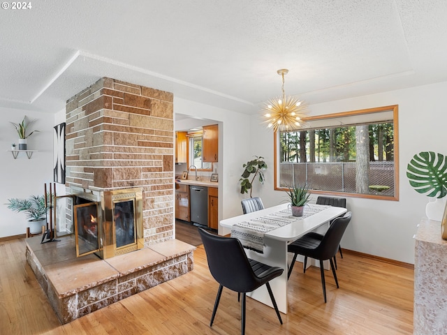 dining area with light wood-style floors, a chandelier, a large fireplace, and a textured ceiling