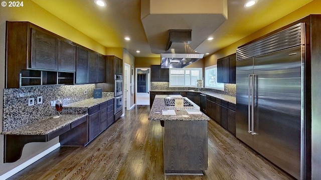 kitchen featuring island range hood, a kitchen island, light stone countertops, stainless steel appliances, and hardwood / wood-style flooring