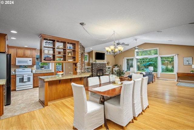 dining room featuring lofted ceiling, a stone fireplace, ceiling fan, and light hardwood / wood-style floors