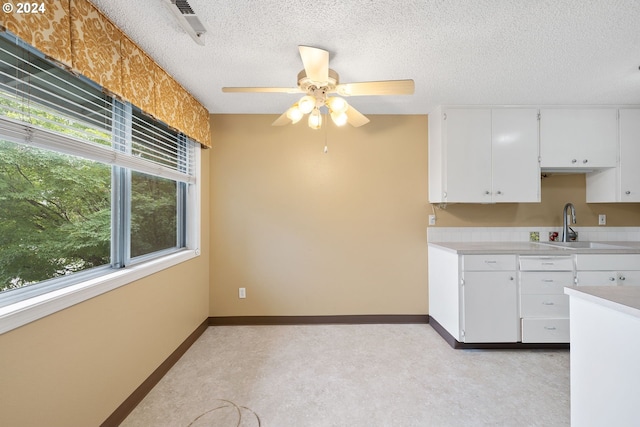 kitchen featuring a textured ceiling, sink, white cabinetry, light colored carpet, and ceiling fan