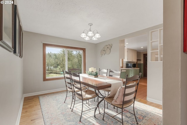 dining space with light wood-type flooring, a textured ceiling, and a notable chandelier