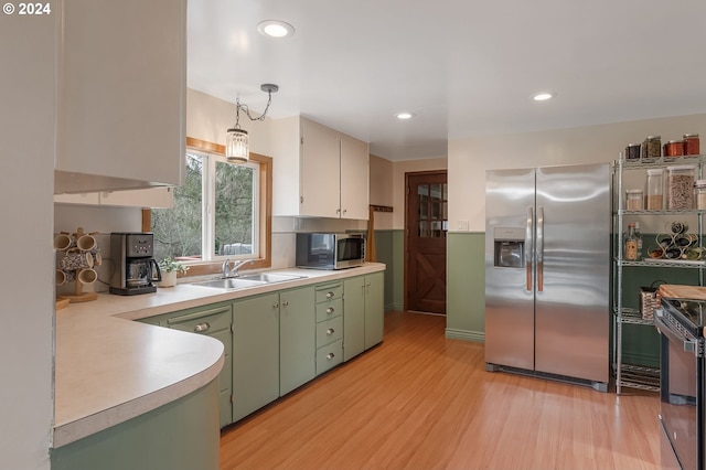 kitchen with green cabinets, sink, light hardwood / wood-style flooring, decorative light fixtures, and stainless steel appliances