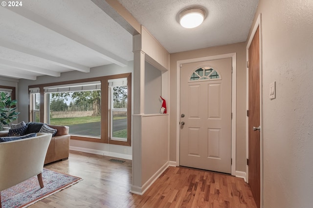 doorway to outside with beam ceiling, a textured ceiling, and light hardwood / wood-style floors