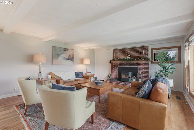 living room with beamed ceiling, light wood-type flooring, a textured ceiling, and a wood stove