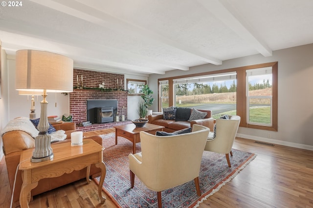 living room with beam ceiling, a wood stove, hardwood / wood-style floors, and a textured ceiling