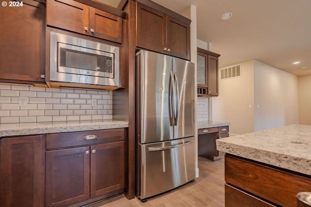 kitchen featuring decorative backsplash, appliances with stainless steel finishes, light hardwood / wood-style floors, and light stone counters