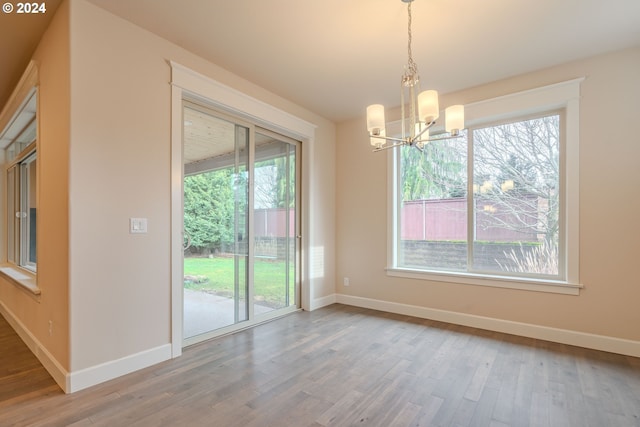 unfurnished dining area featuring a wealth of natural light, wood-type flooring, and a notable chandelier