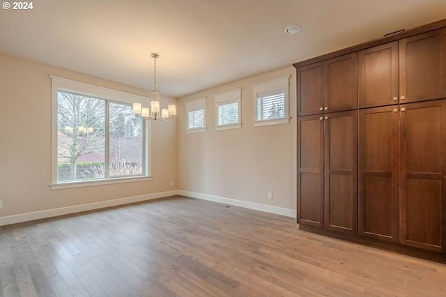 unfurnished dining area featuring light wood-type flooring and an inviting chandelier