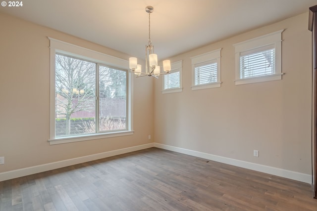 unfurnished room with a wealth of natural light, hardwood / wood-style floors, and an inviting chandelier