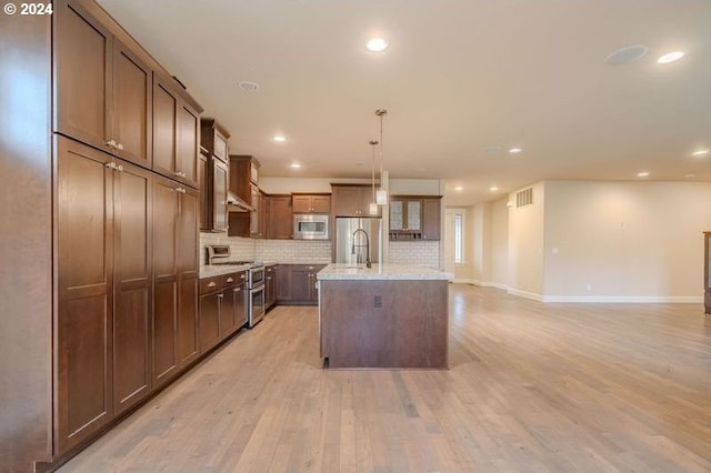 kitchen featuring pendant lighting, a center island with sink, light wood-type flooring, tasteful backsplash, and stainless steel appliances