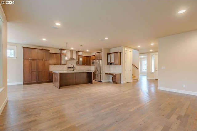 kitchen with pendant lighting, wall chimney exhaust hood, light wood-type flooring, and stainless steel refrigerator