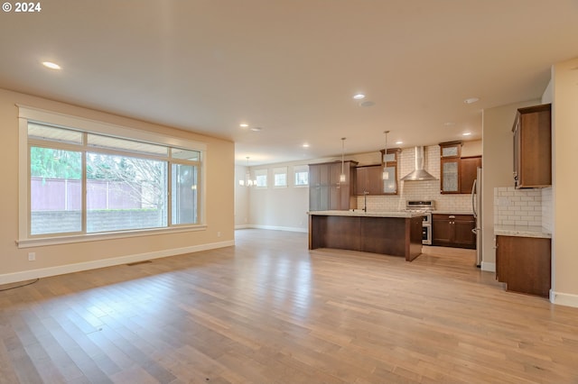 kitchen featuring wall chimney exhaust hood, hanging light fixtures, an island with sink, decorative backsplash, and appliances with stainless steel finishes