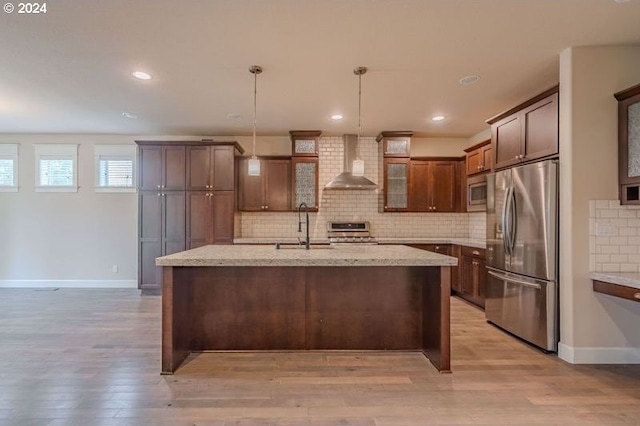 kitchen featuring hanging light fixtures, wall chimney range hood, light stone counters, backsplash, and appliances with stainless steel finishes