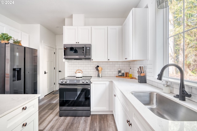 kitchen with appliances with stainless steel finishes, backsplash, light hardwood / wood-style floors, white cabinets, and sink