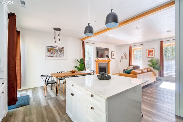 kitchen featuring a center island, pendant lighting, white cabinets, light stone counters, and hardwood / wood-style flooring