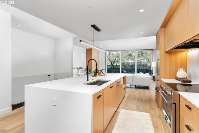 kitchen featuring stainless steel range, a kitchen island with sink, sink, light hardwood / wood-style flooring, and hanging light fixtures