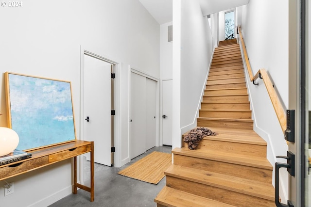 staircase featuring a towering ceiling and concrete floors