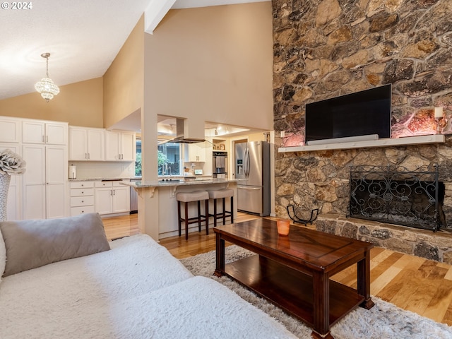 living room with beam ceiling, light hardwood / wood-style flooring, a stone fireplace, and high vaulted ceiling