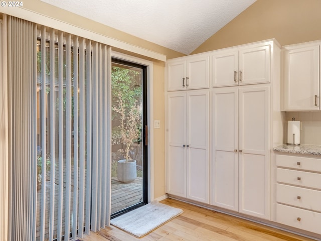 doorway featuring lofted ceiling, light hardwood / wood-style flooring, and a textured ceiling