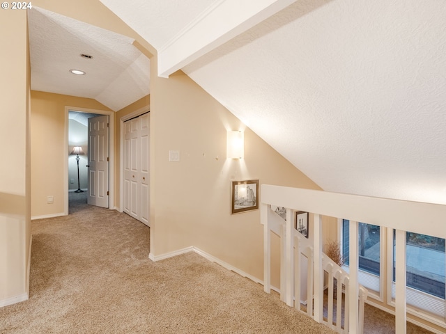 corridor with light carpet, a textured ceiling, and lofted ceiling with beams