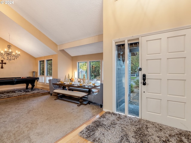 entrance foyer with pool table, a textured ceiling, vaulted ceiling, carpet floors, and a notable chandelier